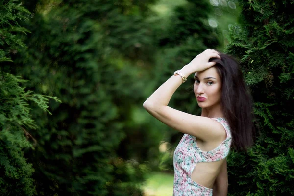 年轻优雅的女士在礼服与花卉打印摆姿势在绿色高的灌木 — 图库照片