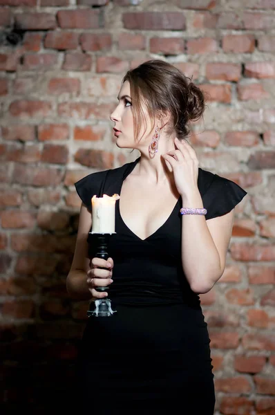 Young elegant woman with candle in hand posing on brick wall background