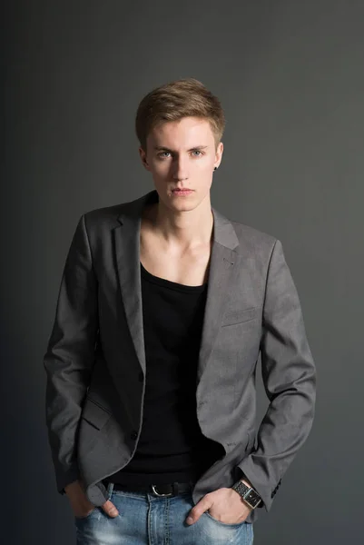 Portrait of young serious man in black t-shirt and stylish blazer posing on grey background