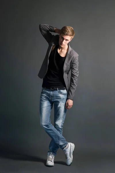 若い男がジーンズでスタイリッシュなブレザー灰色の背景でポーズ — ストック写真