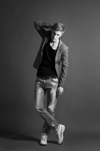 Young man in jeans and stylish blazer posing on grey background