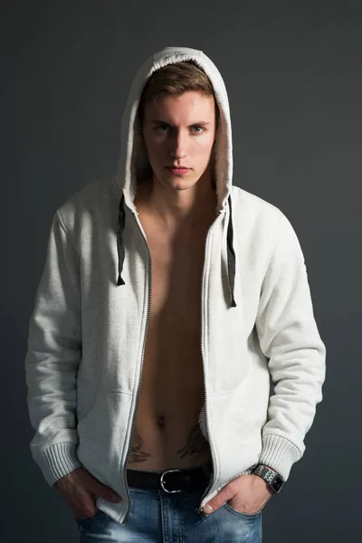 Young man with naked tattooed torso in white hoodie posing on black background