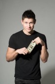 Portrét mladého muže v černé tričko hospodářství dolaru na šedém pozadí