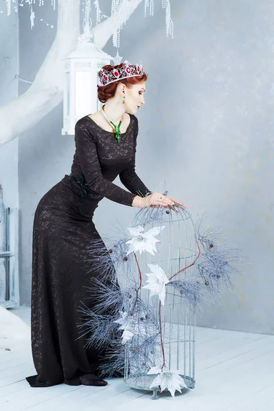 Elegant woman in black dress and ruby crown posing in winter decorated interior