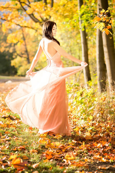 Young woman in elegant pastel pink dress posing in sunny autumn park