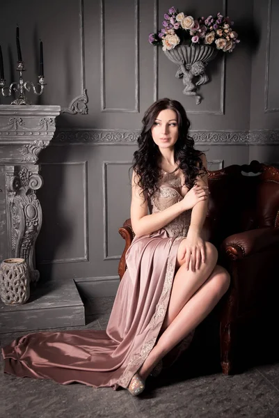Young woman in fancy dress sitting on vintage sofa in luxury interior