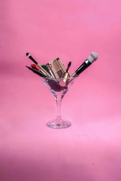 Martini cam pembe bir arka plan üzerinde makyaj araçları