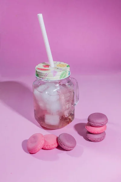 在彩色背景上的马卡龙 彩色的法国马卡龙饼干的图像 马卡龙法式糕点在粉红色的背景下 最小的概念 很多马卡龙树莓柠檬水与冰在玻璃烧杯 用稻草清凉饮料 — 图库照片