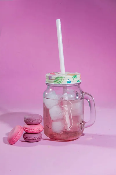 Renkli bir arka plan üzerinde Macaroons, renkli Fransız macarons kurabiye görüntü. Pembe bir arka plan üzerinde Macaron fransız pasta, minimal kavram. Bir sürü makaron. Cam bir kabın içinde buzlu ahududu limonata. Pipetle. Ferahlatıcı içecek.