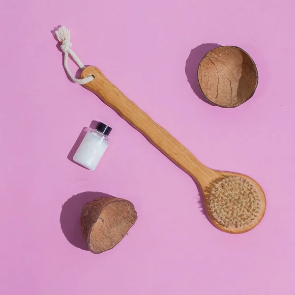 Massage brush. Brush for anti-cellulite massage. On a pink background. With coconut shell. and a bottle of white oil. Accessories for massage.