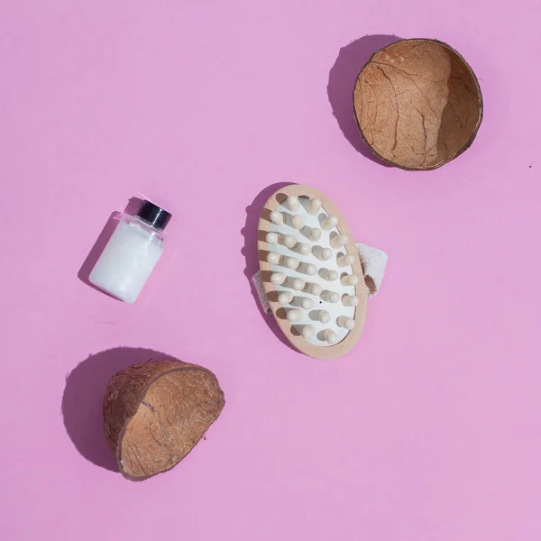 Massage brush. Brush for anti-cellulite massage. On a pink background. With coconut shell. and a bottle of white oil. Accessories for massage.