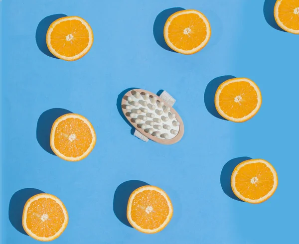 Massage brush without handle. Brush for anti-cellulite massage. On a blue background. With round slices of orange. Hard light, hard shadows.