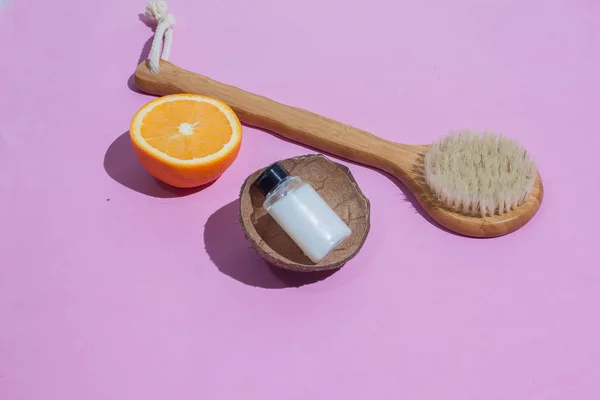 Massage brush. Brush for anti-cellulite massage. On a pink background. With coconut shell. and a bottle of white oil. Accessories for massage.