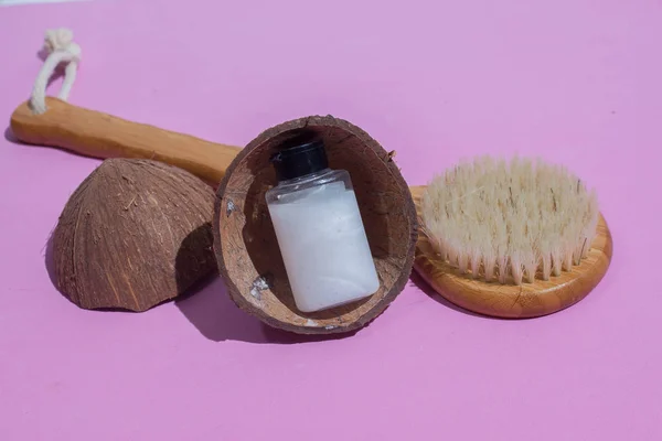 Massage brush. Brush for anti-cellulite massage. On a pink background. With coconut shell. and a bottle of white oil. Accessories for massage.