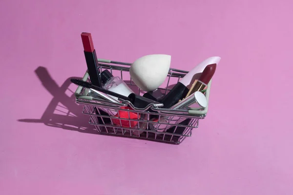 Makyaj ürünleri ile süpermarketten küçük bir sepet. Dekoratif kozmetikler. Pembe arka planda.