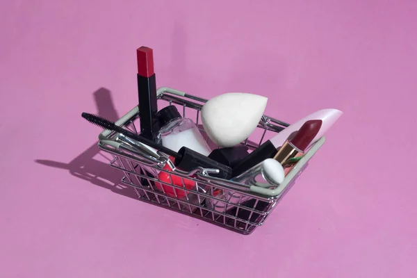 Makyaj ürünleri ile süpermarketten küçük bir sepet. Dekoratif kozmetikler. Pembe arka planda.