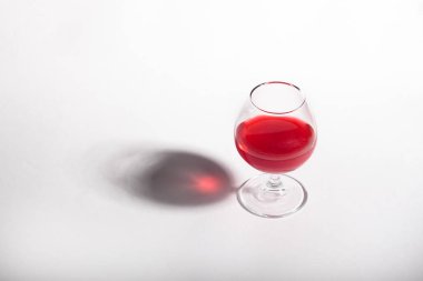 Beyaz arka planda kırmızı içecekli cam kadeh. Minimalizm bir bardak bir gölge ile. 
