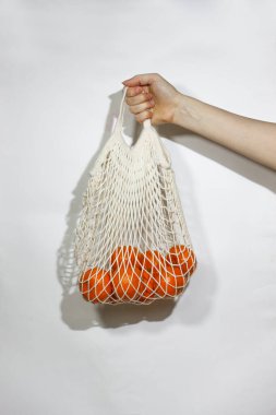 Mandalinalar bir sicim torbasında beyaz bir arka planda kadın ellerinde. Konsept plastik değil. Çevresel bir ürün seçin.  