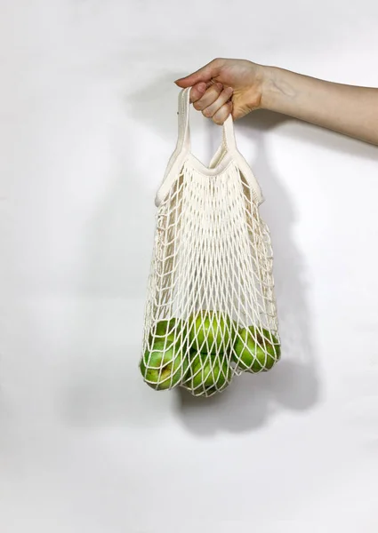 Apples in a string bag in female hands on a white background. The concept is not plastic. Choose an environmental product.