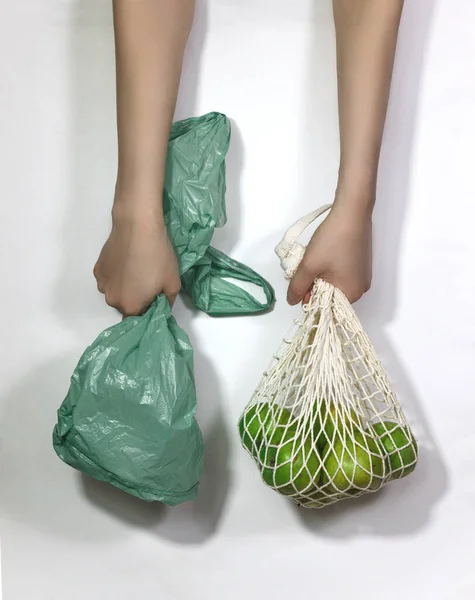 Apples in a string bag and a green plastic bag in female hands on a white background. The concept is not plastic. Choose an environmental product.