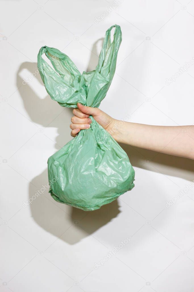 Green plastic bag in female hands on a white background. The concept is not plastic. Choose an environmental product. 