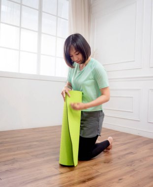 Yeşil yoga veya spor paspası katlayan genç bir kadın.
