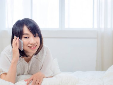 Evdeki bir odanın yatağında cep telefonuyla konuşan güzel Asyalı bir kadının portresi. Genç bir kızla yaşam tarzı ve rahatlama zamanı..