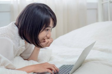 Kadın dizüstü bilgisayarla yatakta yatıyor.