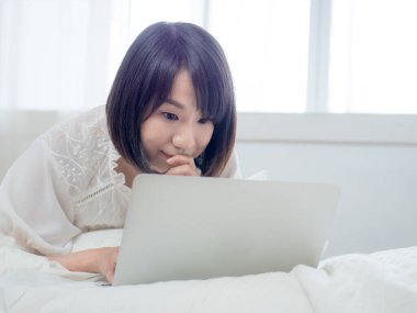 Kadın dizüstü bilgisayarla yatakta yatıyor.