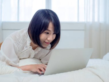 Kadın dizüstü bilgisayarla yatakta yatıyor.