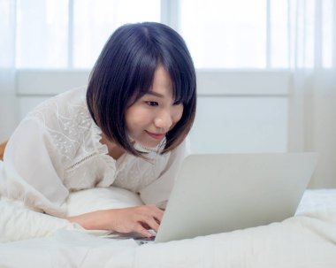 Kadın dizüstü bilgisayarla yatakta yatıyor.