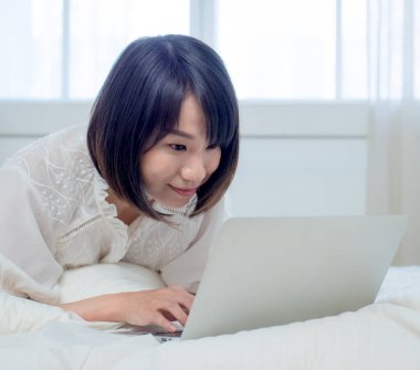 Kadın dizüstü bilgisayarla yatakta yatıyor.