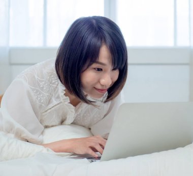 Kadın dizüstü bilgisayarla yatakta yatıyor.