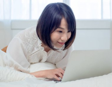 Kadın dizüstü bilgisayarla yatakta yatıyor.