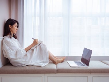 Güzel bir Asyalı kadın bir kitaba bir şeyler yazar.