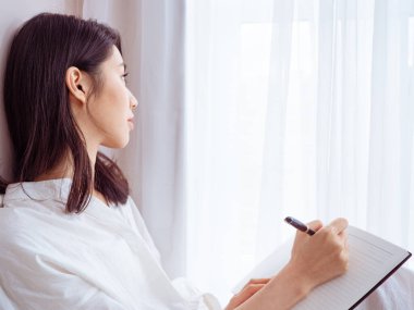 Güzel bir Asyalı kadın bir kitaba bir şeyler yazar.