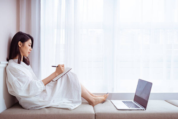 A beautiful Asian women writes something in a book