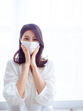 Grip hastası genç Asyalı kadın evde cerrahi maske takıyor.