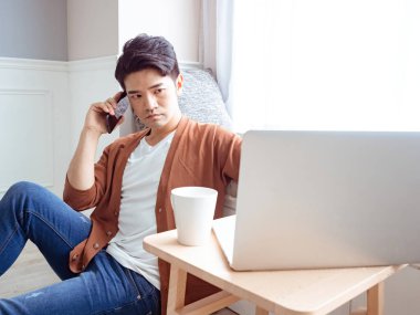 Gündelik kıyafetler giyen ve cep telefonuyla konuşan genç bir adam.