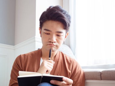 Genç Asyalı bir adam bir kitaba yazıyor.