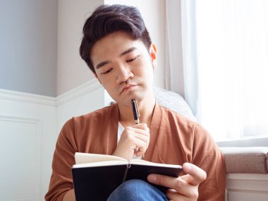 Genç Asyalı bir adam bir kitaba yazıyor.