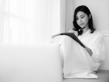 Güzel bir Asyalı kadın siyah beyaz bir kitap yazar.