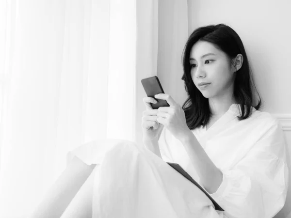 Genç Asyalı Kadın Evde Siyah Beyaz Akıllı Telefon Kullanıyor — Stok fotoğraf