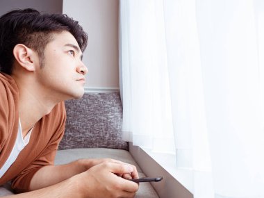 Genç adam günlük kıyafetler giyiyor ve evde akıllı telefon kullanıyor.