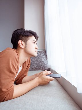 Genç adam günlük kıyafetler giyiyor ve evde akıllı telefon kullanıyor.