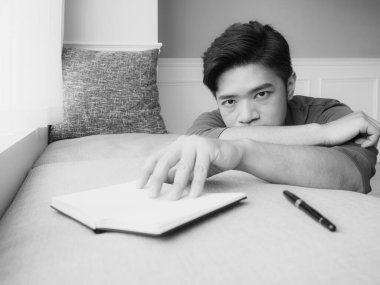 Genç Asyalı adam evde siyah beyaz kitap okuduktan sonra ara veriyor.