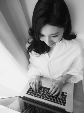 Genç Asyalı kadın evde siyah beyaz bilgisayar kullanıyor.