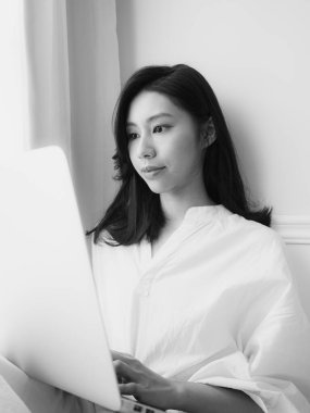 Genç Asyalı kadın evde siyah beyaz bilgisayar kullanıyor.