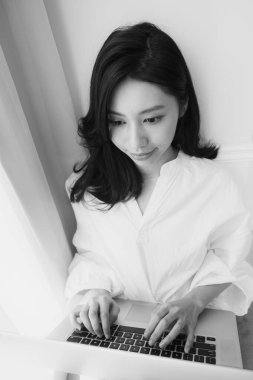 Genç Asyalı kadın evde siyah beyaz bilgisayar kullanıyor.