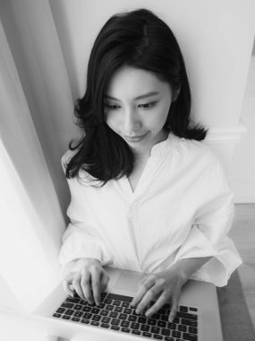 Genç Asyalı kadın evde siyah beyaz bilgisayar kullanıyor.